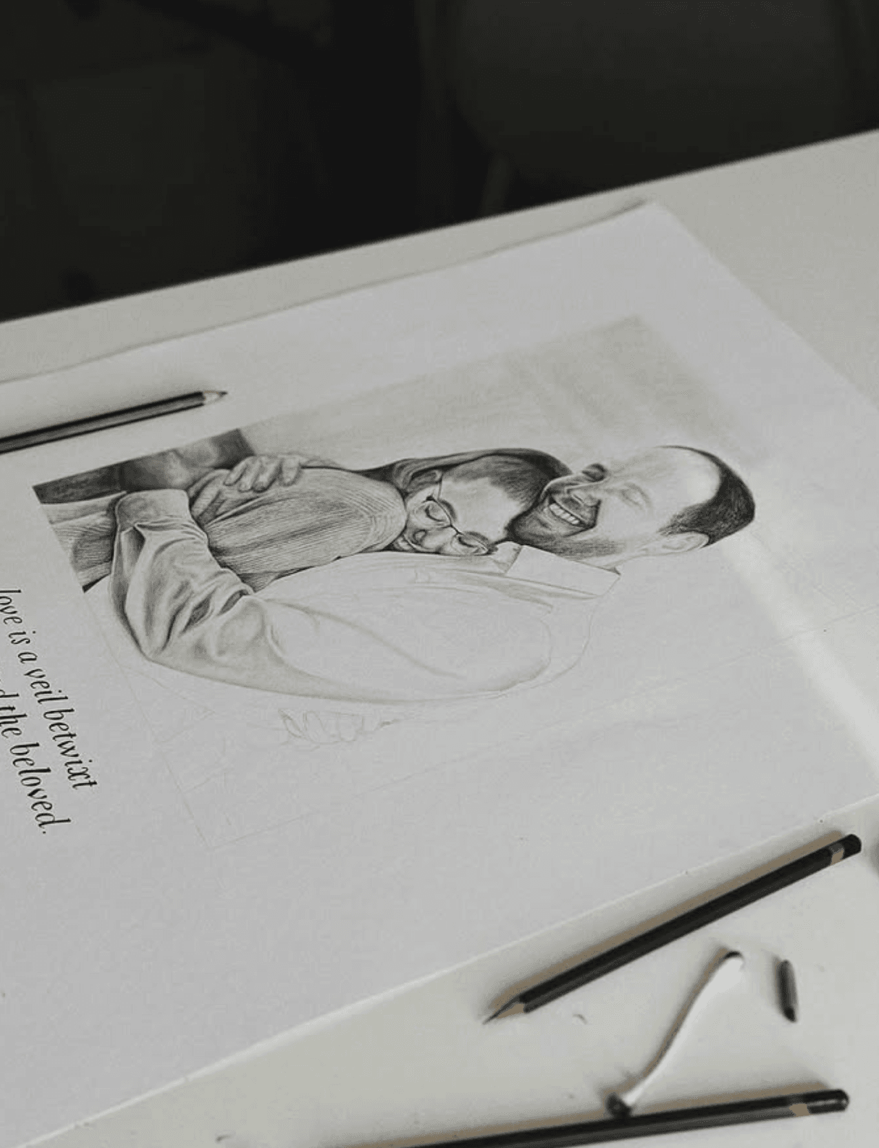 Pencil portrait of a couple mid-laugh, drawn by hand with pencils resting beside the sketchbook