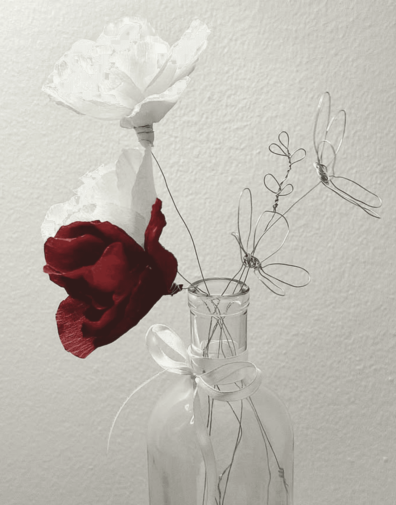 Handmade crepe-paper roses in white and deep crimson with delicate wire flowers in a glass bottle