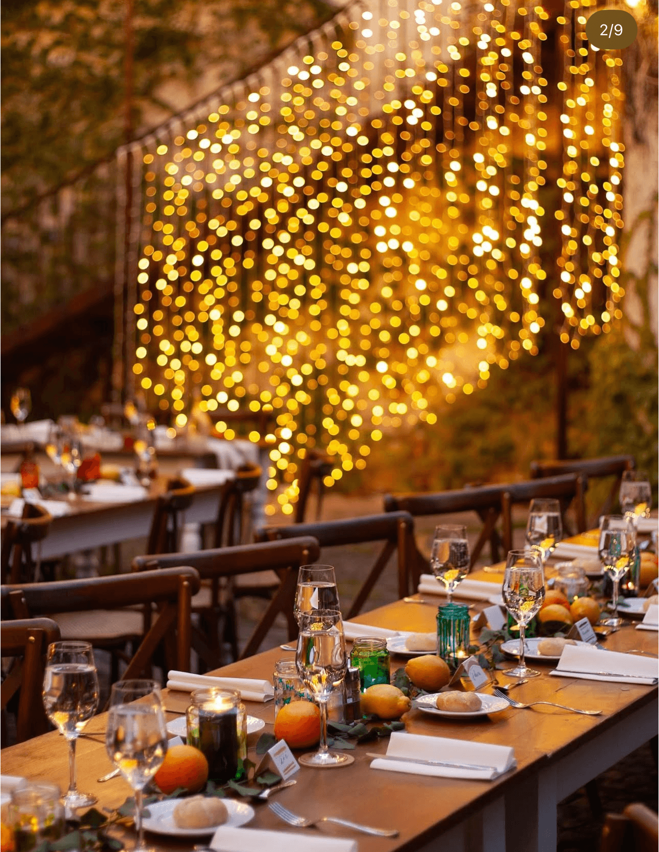 Curtain of warm fairy lights glowing above long candlelit dinner tables dressed with citrus and greenery