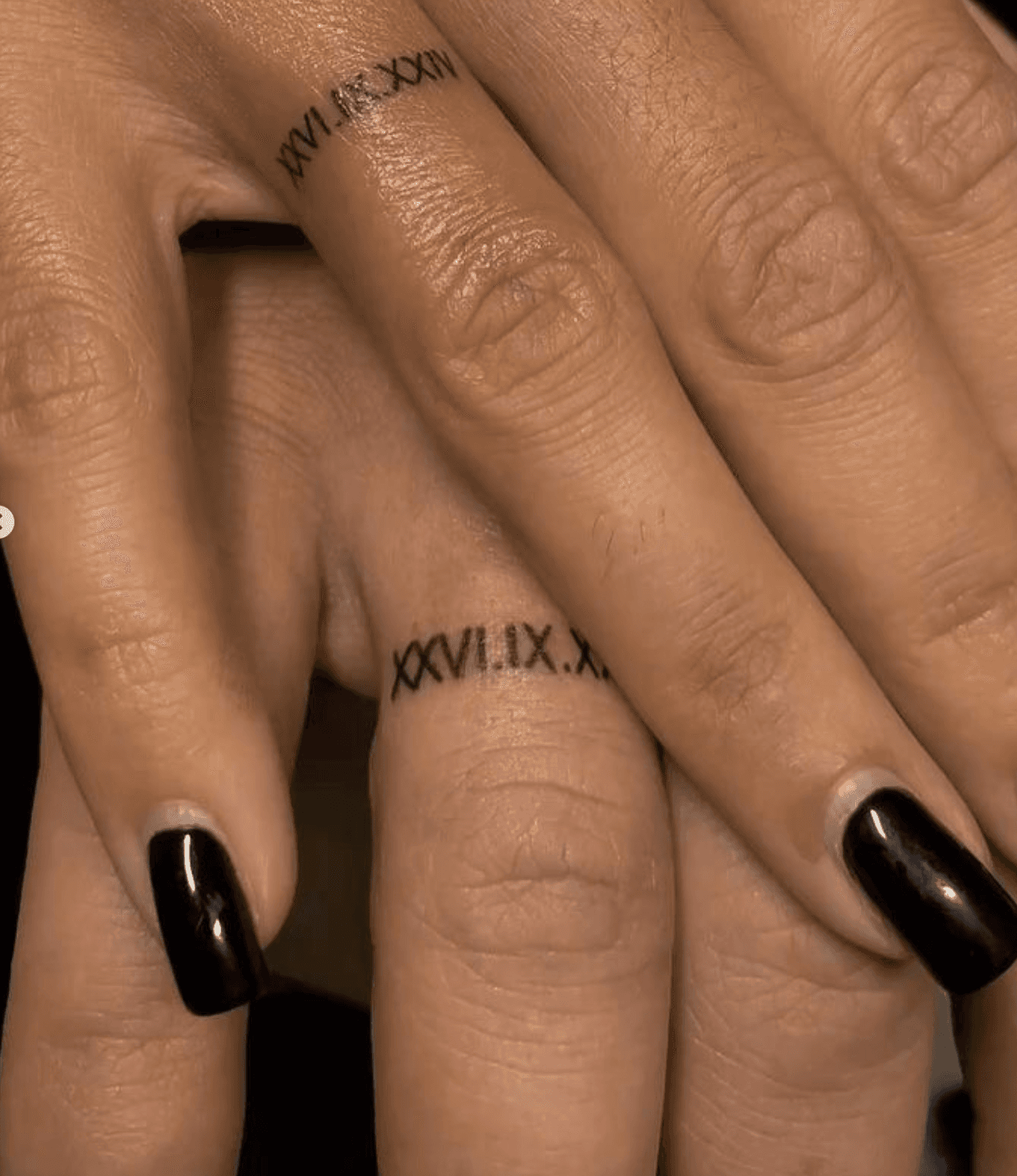 Two hands with matching fine-line roman numeral date tattoos on the ring fingers
