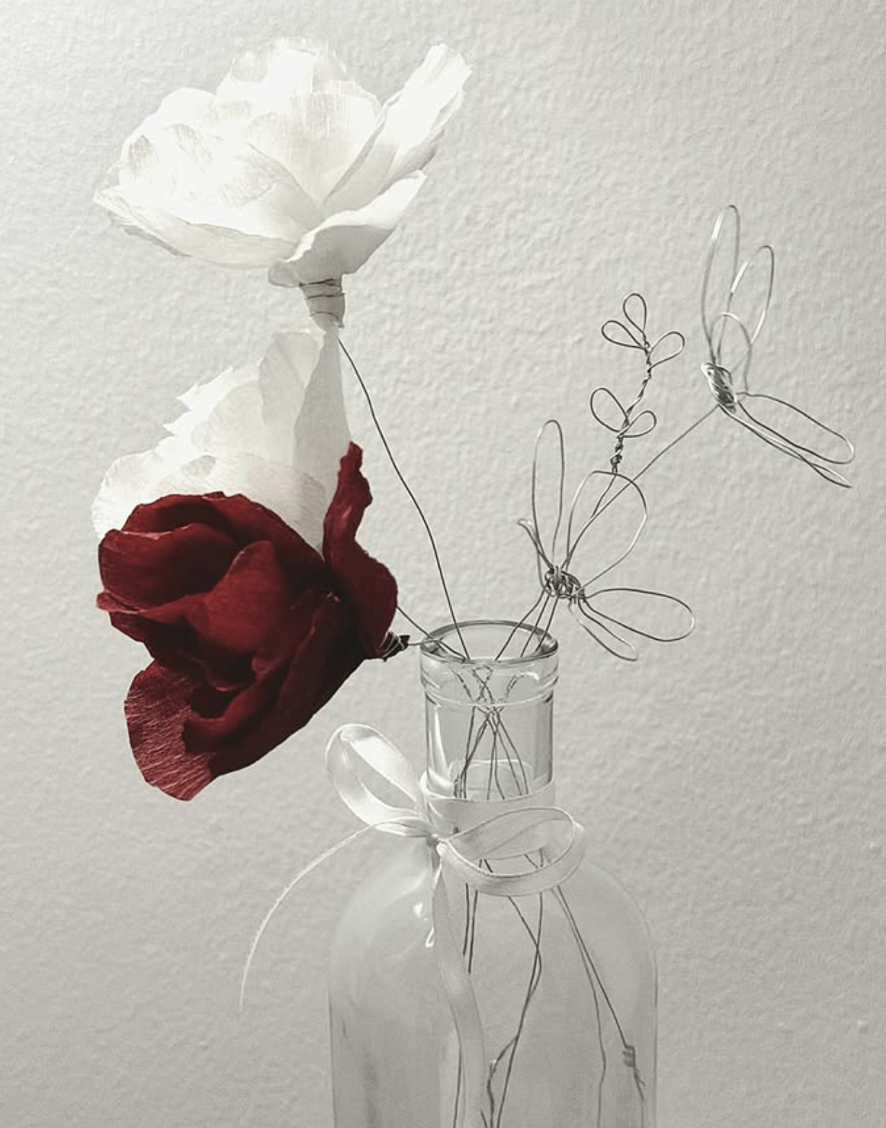 Handmade crepe-paper roses in white and deep crimson with delicate wire flowers in a glass bottle