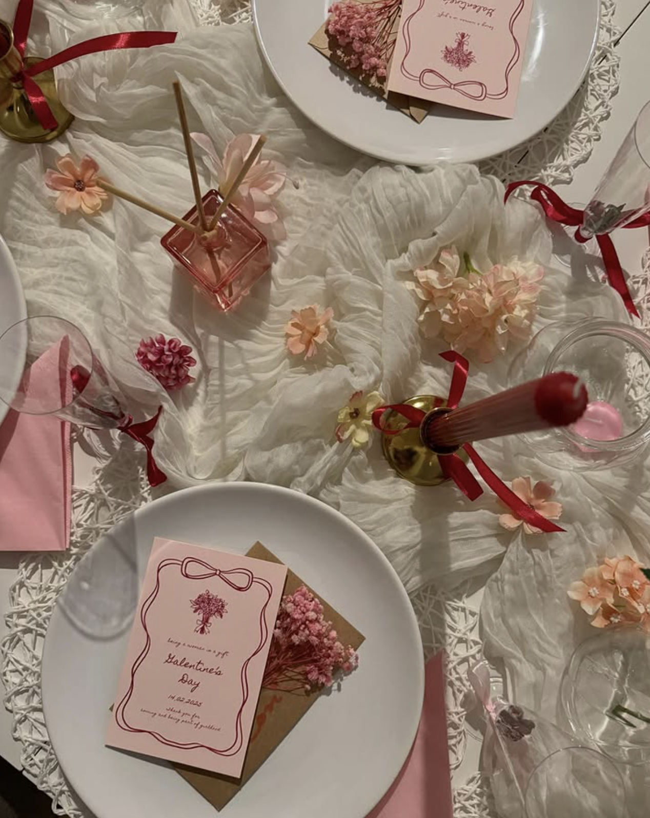 Hand-illustrated pink place cards with crimson ribbon borders, dried flowers and candles on a layered tablescape