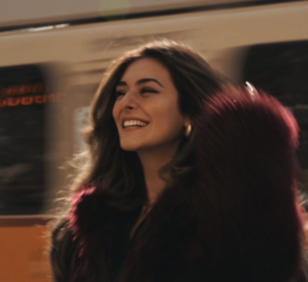 Portrait of the founder smiling in a deep red coat, hair catching the light
