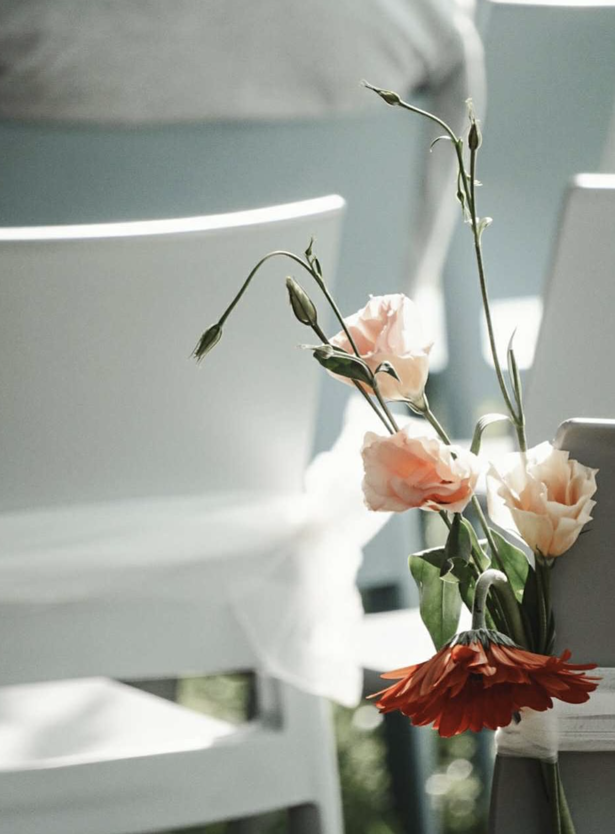 Peach and terracotta ceremony flowers tied to the back of a white chair