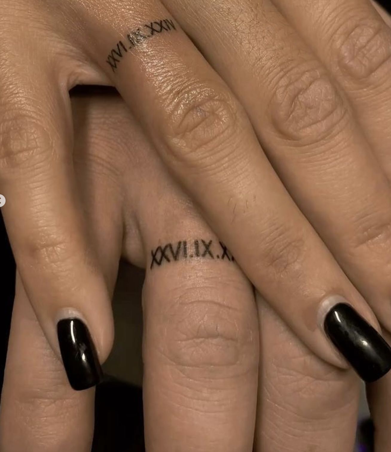 Two hands with matching fine-line roman numeral date tattoos on the ring fingers